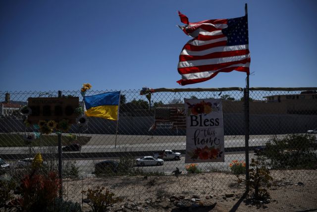 A flag of the United States waves in the wind with a flag of Ukraine, along a fence outside Los Angeles