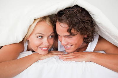 Couple under a duvet with a knowing smile in a bed